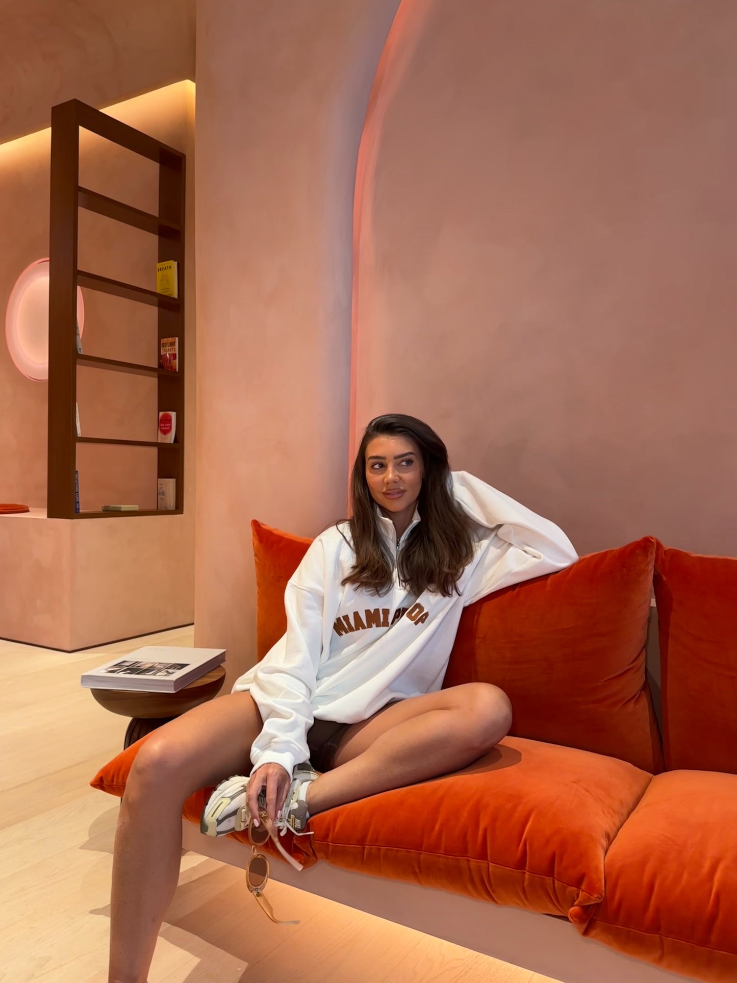 Woman sitting on an orange couch in a modern room with a pink wall.